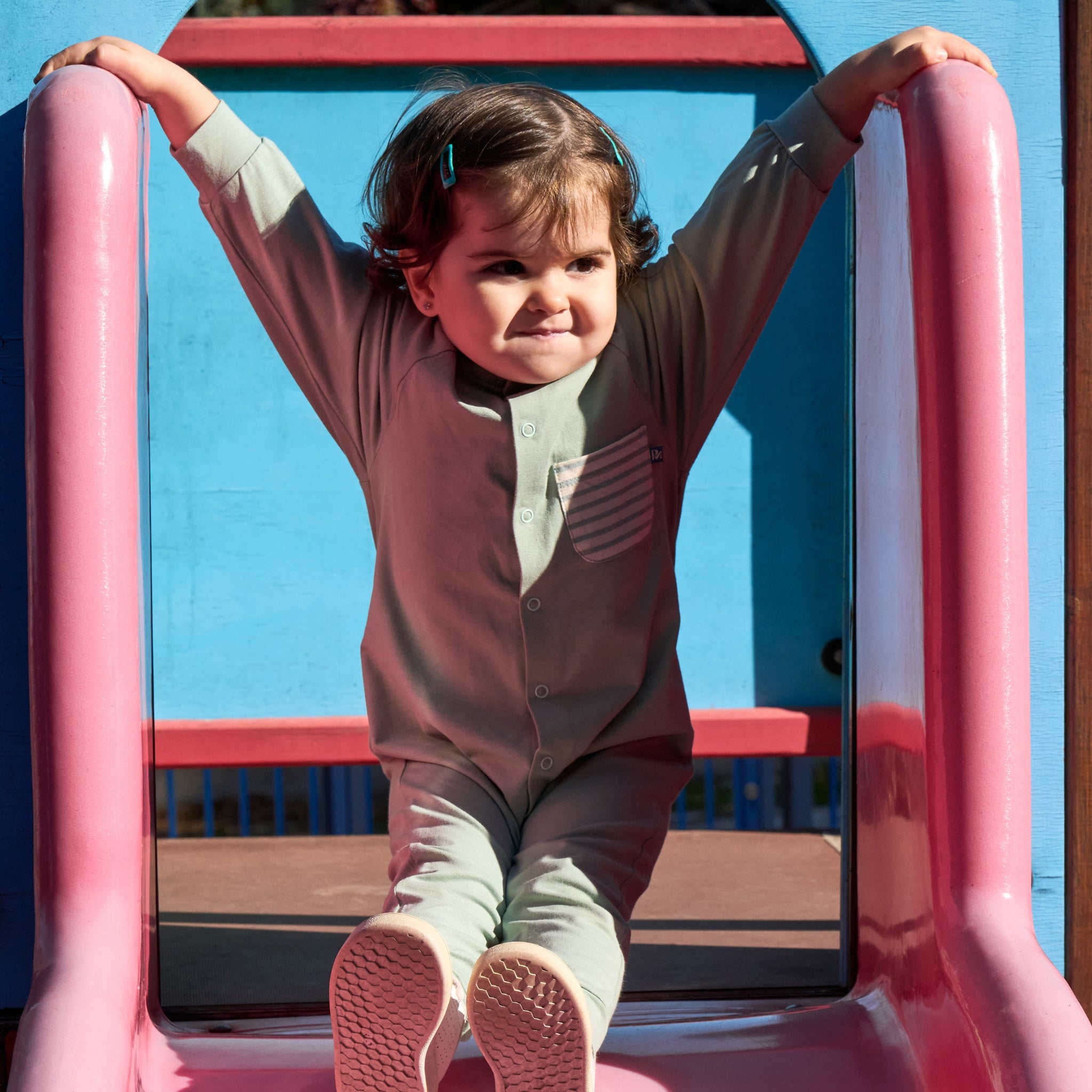 Ein Kind steht am Anfang einer bunten Rutsche, hält sich links und rechts fest und trägt einen UPF50+ Overall.